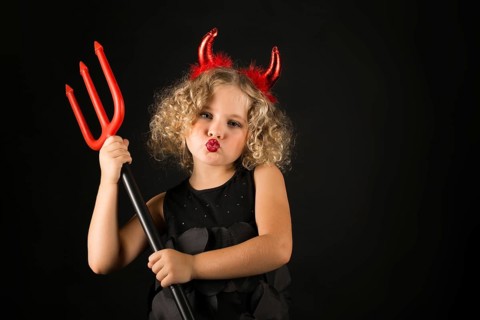 Isolated on black, adorable caucasian blonde little girl in black dress, with red horns on head