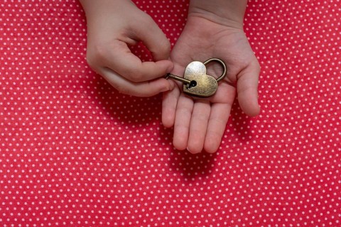 Hand holding a heart shaped lock and key on a red background