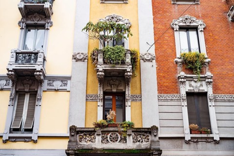 Facade of the building with stucco, balconies and flowerpots. Milan, Italy.