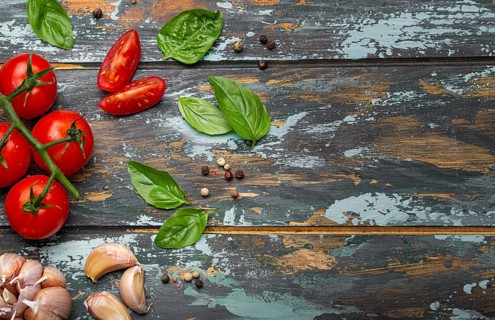 Food cooking border with cherry tomatoes, fresh green basil and garlic cloves top view on rustic