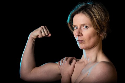 Low key studio portrait of a 35 year old white woman with naked shoulders showing her biceps,