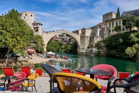 Cafe with colourful chairs on the bank of the river Neretva, behind the bridge Stari Most, numerous