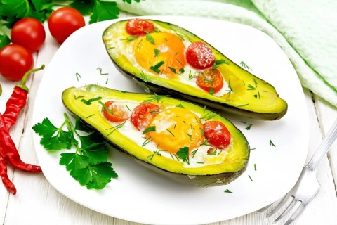 Scrambled eggs with cherry tomatoes in two halves of avocado in a plate, kitchen towel and fork on