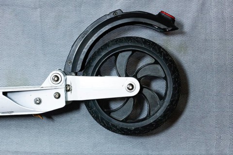 Close-up of a scooter's rear wheel with a sleek black tire and metal frame on a grey background