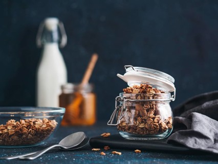 Homemade granola in glass jar on dark table. Ingredients for healthy breakfast - granola, milk and
