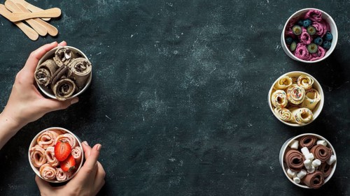 Hands with rolled ice cream in cone cups on dark background. Different iced rolls top view or flat
