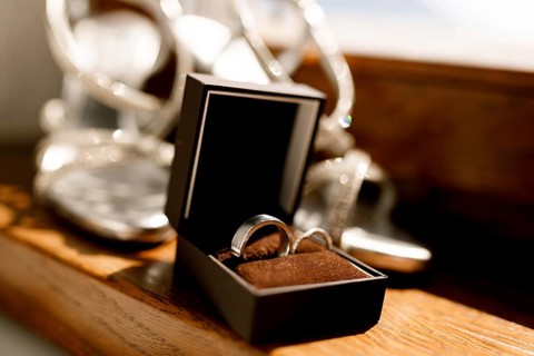 Wedding rings in an open brown box on the floor with women's wedding sandals on a blurred