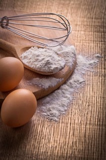 Flour in spoon eggs and corolla on vintage wooden board food and drink concept