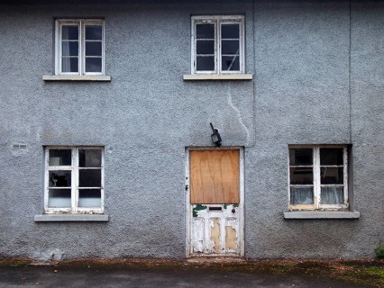 An old abandoned grey derelict house on a residential street with dirty broken windows and a