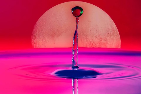A drop of water rises into the air in front of a large full moon and in a pink-red sky, Planet