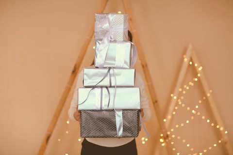 Female holding big stack of presents wrapped in brown paper with white bows on simple background
