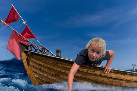 Child in a wooden boat with waves and holding his hand in the water