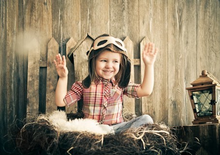Happy kid playing in pilot helmet near the wooden background