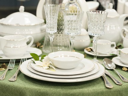 Set of new dishes on table with green tablecloth. Stack of white plates with flowers on restaurant