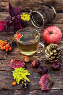 Transparent cup with herbal tea on the table strewn with autumn leaves, chestnuts and pine cones