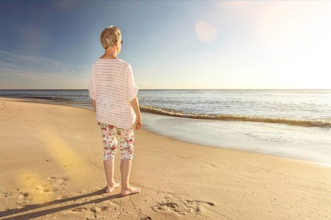 Older woman standing at the beach and looking towards the ocean with scenic lens flare