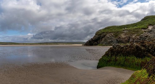 View of the picturesque golden sand Maghera Beach with algae-covered rocks and cliffs in the