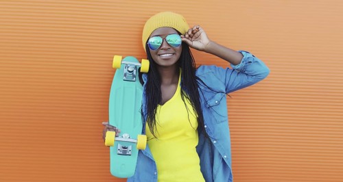 Summer portrait of stylish happy African young woman with skateboard, modern black teenage girl in