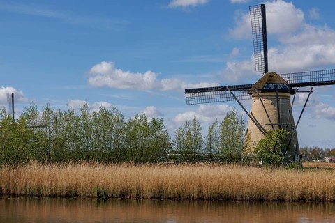 A traditional windmill in a wide landscape with meadow, water and cloudy sky on a summer's day,