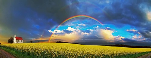 Panorama, chapel and rainbow over a rapeseed field