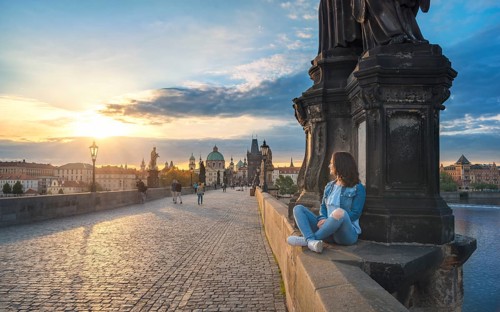 Young brunette woman, sitting relaxed on the Charles Bridge walls, over the Vltava river, admiring