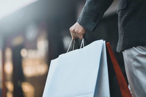 Close up of a young caucasian man holding some different paper shopping bags in the street