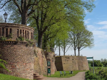 Defence defence tower and brick wall along a walkway, flanked by trees and park benches under a