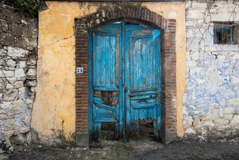 Entrance of an abandoned house with a blue damaged wooden door from a traditional house in Cyprus