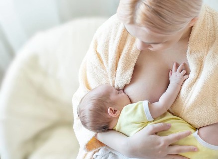 Baby eating breast milk. Caucasian blonde young mother breastfeeding her baby horizontal photo.
