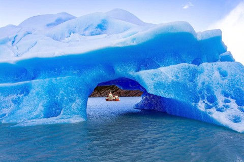 Huge iceberg has broken off from the Gray Glacier and drifts across the lake. Boat with tourists
