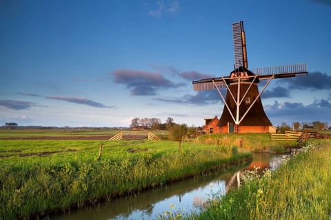 Dutch windmill reflected in river in morning sunrise sunlight, Holland