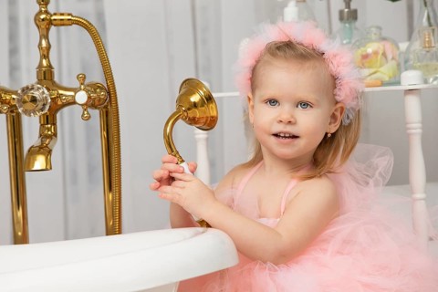 Little funny girl in a smart pink dress in the bathroom