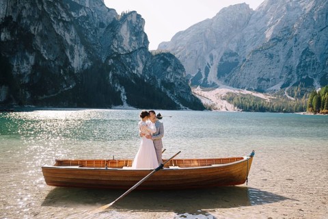 Bride and groom sailing in wooden boat, with oars at Lago di Braies lake in Italy. Wedding in