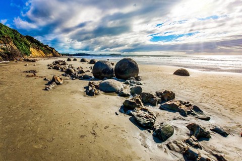 Sunny day on the beach. Low tide in the Pacific. Series of mysterious round boulders Moeraki and