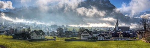 Panorama over the village of Schwyz, Switzerland with wisps of fog and clouds in oblique sunlight,