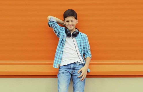 Portrait of happy modern teenage boy listening to music with headphones in the city on orange wall