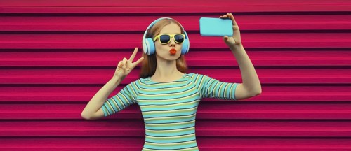Summer portrait of stylish young woman taking selfie with smartphone listening to music with