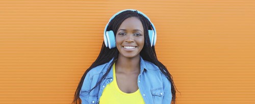 Portrait of happy African young woman listening to music with headphones, cool modern black teenage