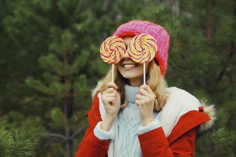 Winter portrait of happy funny smiling young woman having fun with sweet lollipop wearing hat