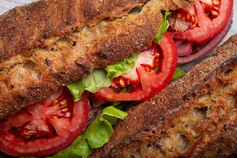 Close-up macro of dark ciabatta sandwich with green salad, ripe red tomatoes and tuna. Vegetable