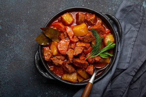Beef meat stew with potatoes, carrot and delicious gravy in black casserole pot with bay leaves and