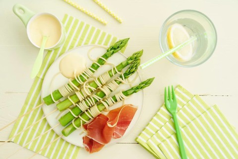 Steamed green asparagus on wooden skewers with spaghetti wrapped in hollandaise sauce and ham