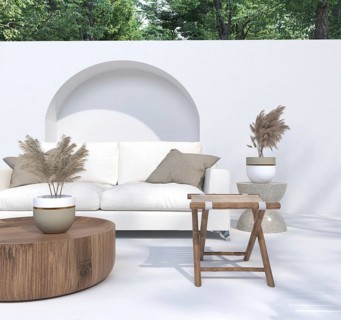 Outdoor seating area with a white sofa, potted plants, and wooden table under bright light