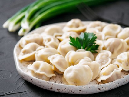 Traditional russian pelmeni, ravioli, dumplings with meat on black concrete background. Russian