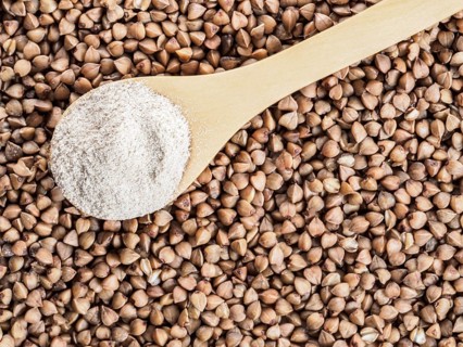 Buckwheat flour in wooden spoon and buckwheat grains. Whole-grain buckwheat flour on buckwheat