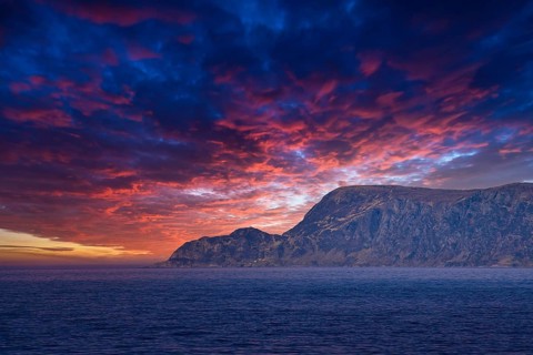 View from the sea to the West Cape in Norway at sunset with sun rays and heavy clouds. Waves in the