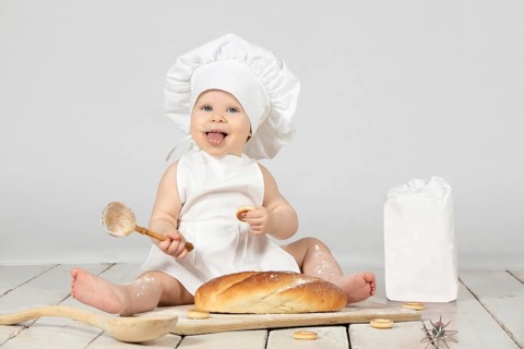 Child cooking. Beautiful little girl in cooking clothes with a long loaf of bread and flour. The