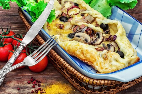Baking with dough with meat and mushrooms in glass form and kitchen fork and knife