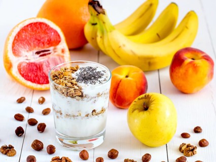 Healthy breakfast: yogurt with muesli and chia seeds, fruits and nuts on white wooden background.