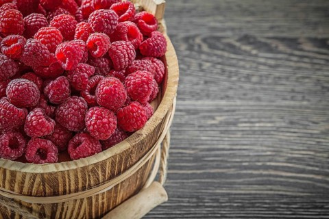 Raspberries in bucket on vintage wooden board horizontal image